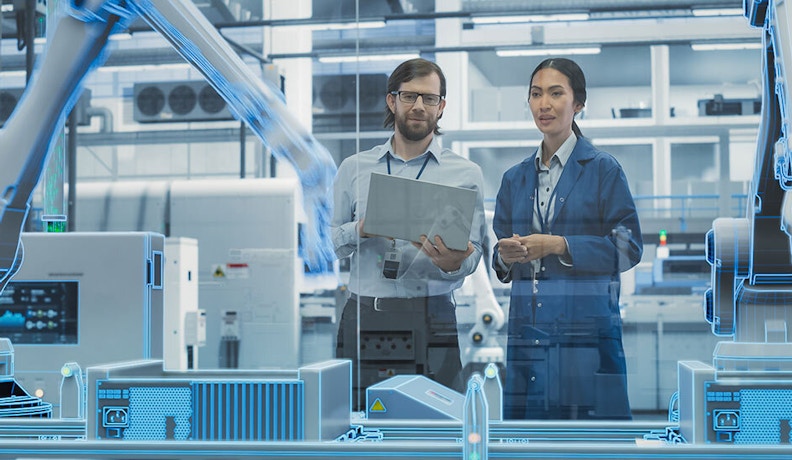 Engineers using digital tools in an AI-enabled manufacturing environment Engineers in a smart factory reviewing data on a tablet with robotic equipment in the background.