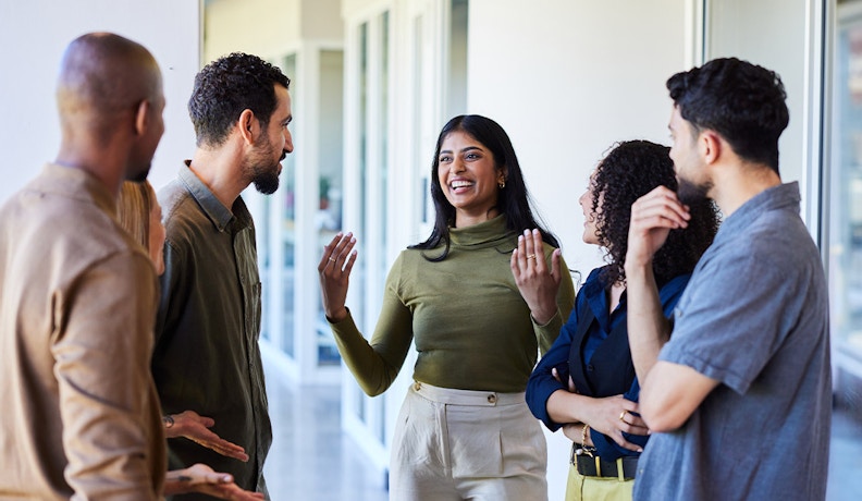Employee Wellness Programs Through Team Bonding Coworkers chatting and smiling in a bright office hallway, discussing employee wellness programs.