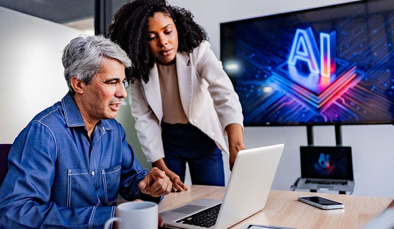 Small Business Team Using AI Technology in Office Two professionals discussing AI strategies for small business on a laptop, with an AI graphic on a screen in the background.