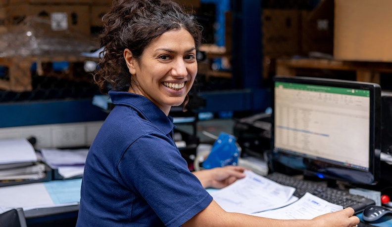 AP Automation in Warehouse Office Workflow A woman working with invoices and spreadsheets in a warehouse office, illustrating AP automation in action.