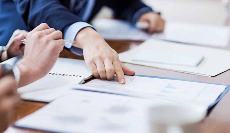 CMMC Compliance Myths Discussed in Business Strategy Meeting Close-up of business professionals reviewing documents during a meeting about CMMC compliance myths and strategies