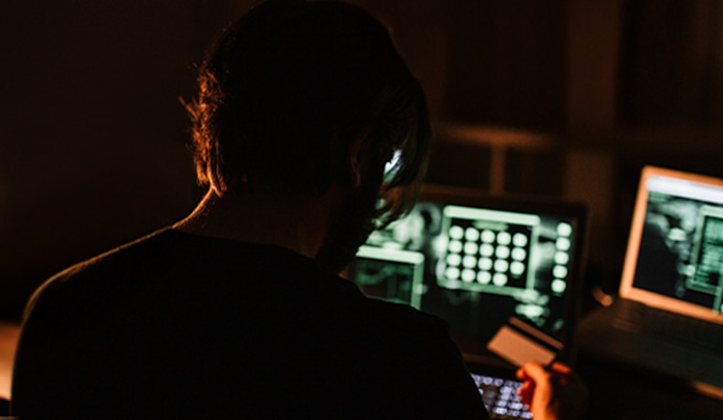 Credit card fraud prevention for businesses credit card fraudster in a dark room attempting to use a stolen credit card online