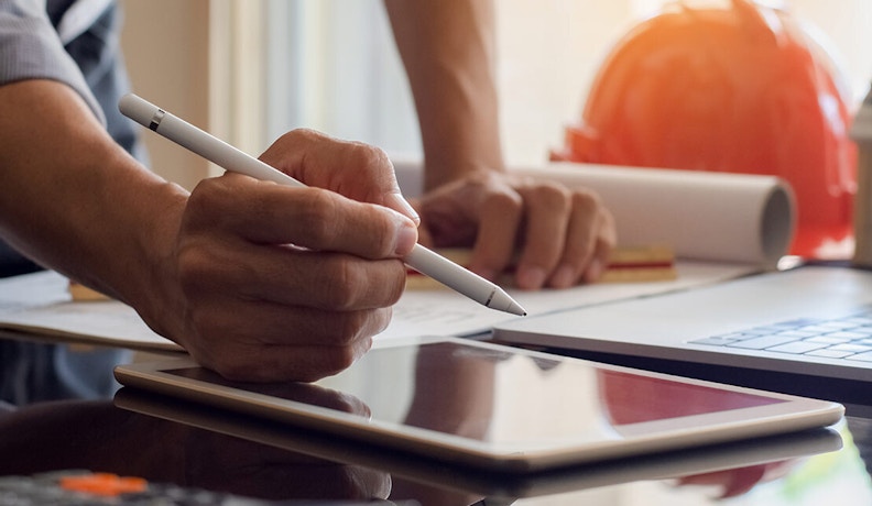 Improving Document Management In Residential Construction Construction professional using digital tablet and laptop for project document management in residential construction