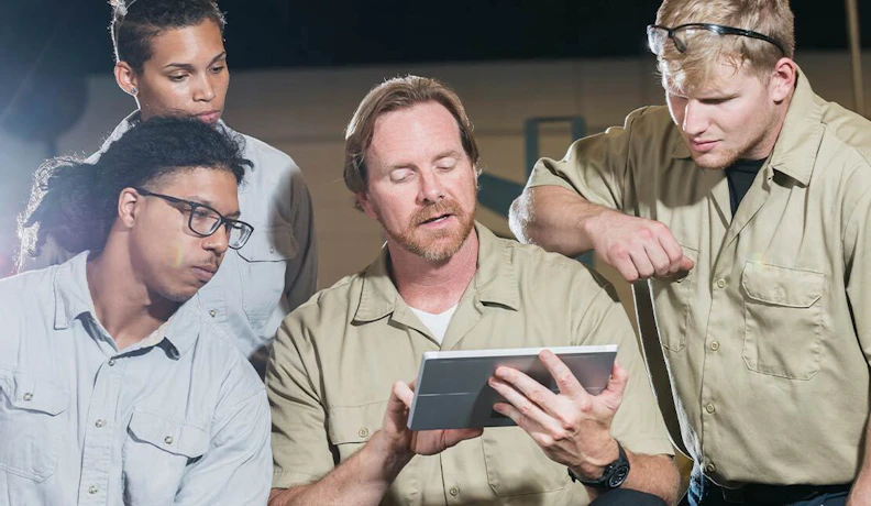 ERP End-User Training Session Using Tablet Technology A group of industrial workers gathered around a trainer reviewing ERP software on a tablet during a training session.