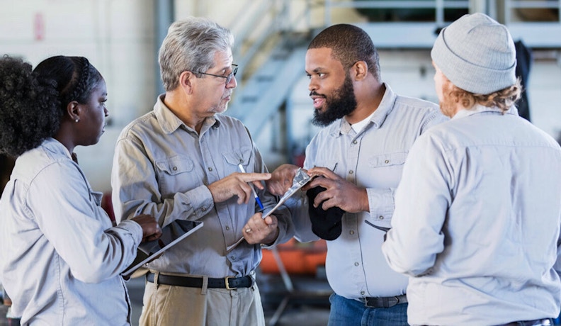 Harness Momentum in Business Through Team Collaboration Four industrial workers in discussion, actively collaborating and sharing tools to harness momentum in business as a team.