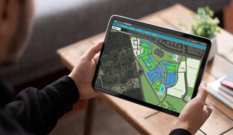 Interactive LotVue Community Map on Tablet Person using a tablet to view an interactive LotVue community map with color-coded housing sections and satellite overlay