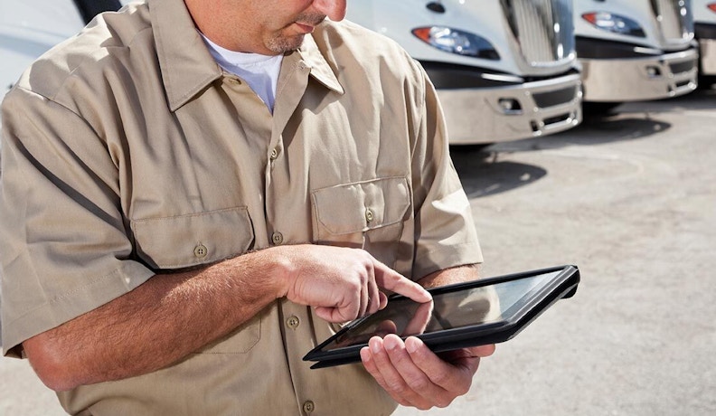 Driver Using Proof of Delivery Software on Tablet A delivery driver in a khaki shirt uses a tablet for proof of delivery with trucks in the background.