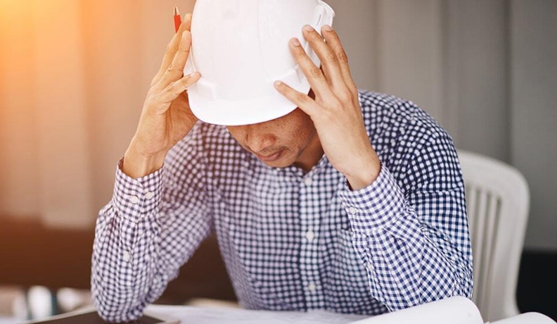 Stressed Engineer Reviewing Residential Project Plans Frustrated engineer in hard hat reviewing papers, reflecting challenges of residential construction management software.