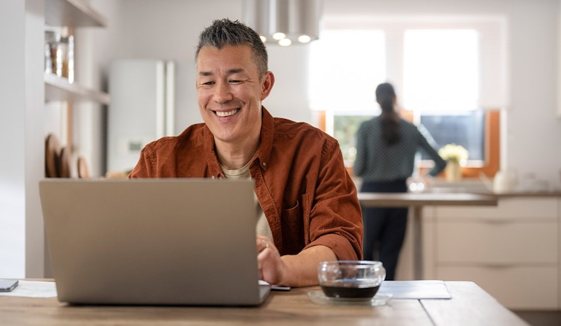 Scaling a Side Hustle to a Million-Dollar Online Business Smiling man working on a laptop at home, representing the journey of scaling a side hustle into a million-dollar business.