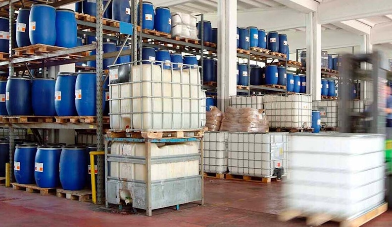 ERP System Streamlining Chemical Inventory Management A chemical manufacturing warehouse with stacked blue barrels and IBC tanks, showing inventory operations supported by an ERP system.