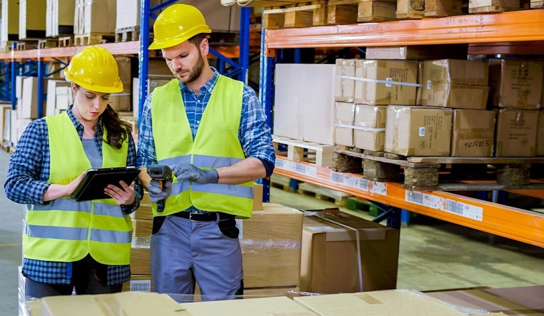 Ecommerce Tools Empowering Industrial Safety Distributors Two warehouse workers in safety gear using a tablet and barcode scanner to manage MRO inventory, showcasing ecommerce efficiency.