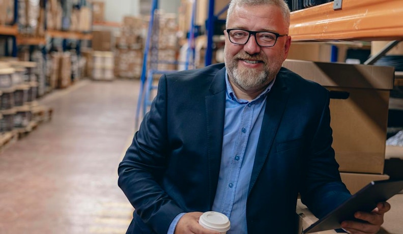 B2B Ecommerce Features Streamlining Distributor Operations Smiling distributor in a warehouse using a tablet, showcasing B2B ecommerce tools for inventory and order management.