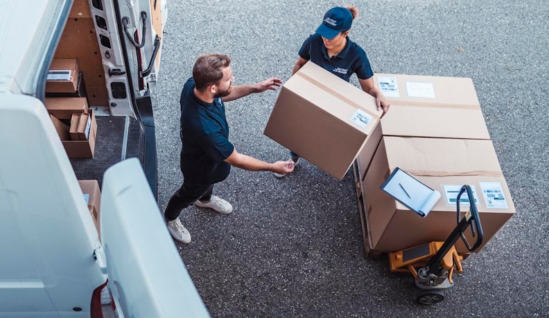 Delivery Management Software in Action: Efficient Parcel Handling Two delivery workers loading boxes from a pallet into a van, illustrating efficient logistics with delivery management software.