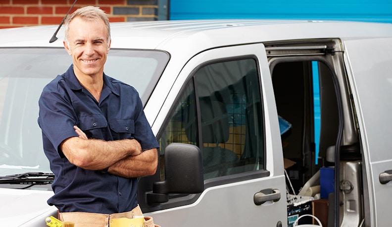 GPS Tracking Solutions for Construction Equipment Fleets Smiling technician in uniform standing beside a work van, representing GPS tracking services for construction equipment.