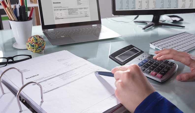 Hidden Costs of Manual Accounts Receivable Processing Person using a calculator to review printed invoices, highlighting the manual process and inefficiencies of accounts receivable tasks.