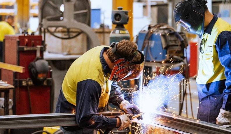 Building Team Buy-In: Collaboration in a Welding Workshop Two workers in safety gear welding metal in a workshop, illustrating teamwork for achieving sales team buy-in in ecommerce.