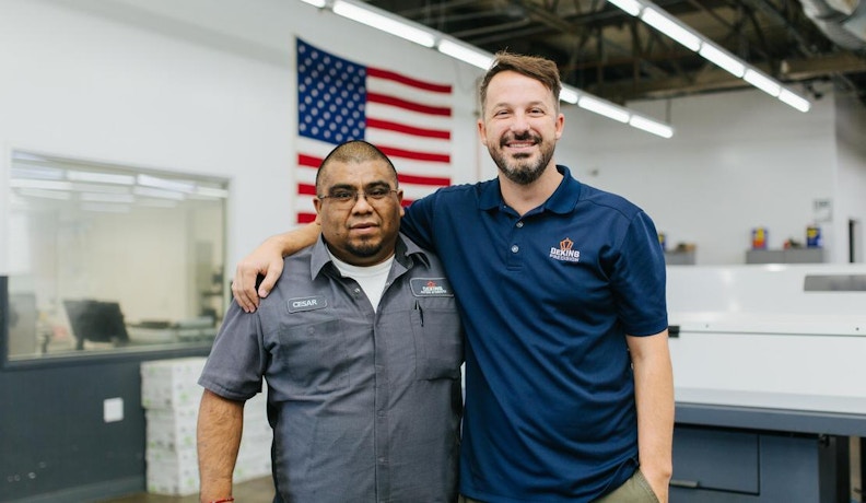 JobBOSS² Training and Support for Job Shop Teams Two job shop workers smiling and posing in a manufacturing facility, highlighting JobBOSS² support resources.