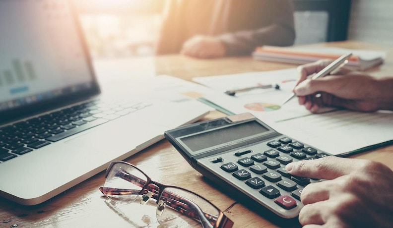 Section 179 Tax Deduction for Small Business Equipment Hands using a calculator and writing on financial documents beside a laptop, illustrating Section 179 tax deduction planning.