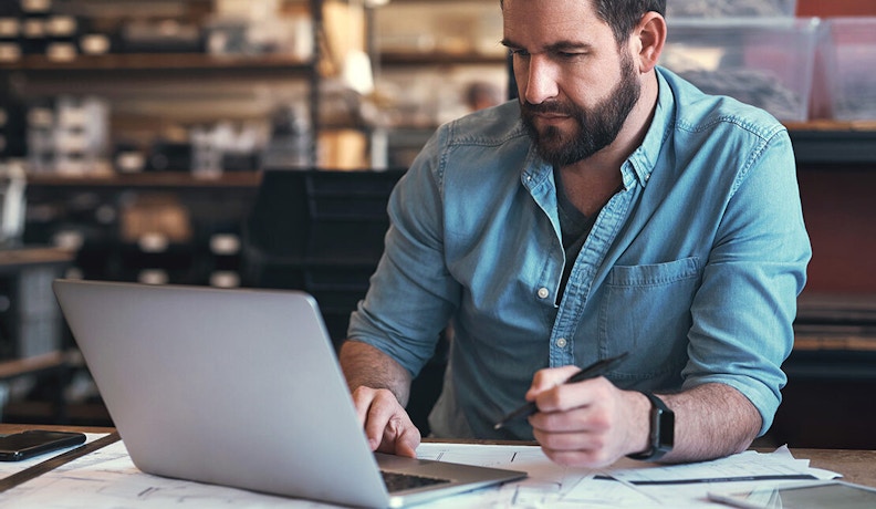 Trade Contractor Reviewing Profit Checkup Data A trade contractor analyzing profit checkup reports on a laptop at a workbench.